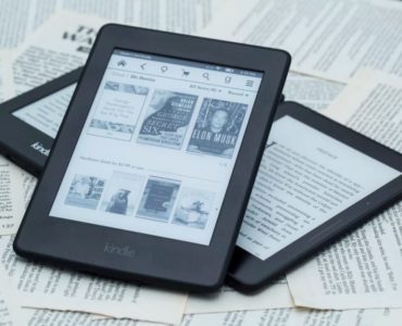 Czytniki Kindle ustawione na sobie, które wyświetlają bibliotekę czytnika oraz e-book.