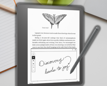 Kindle Scribe leżący na biurku, w tle laptop oraz notatnik.